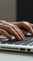 Close-up of hands typing on a laptop keyboard, vertical image