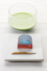 Cup of fresh matcha tea, green tea and Kingyoku can, traditional Japanese jelly confectionery on white wooden table.