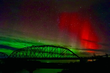 red northern lights aurora borealis over a truss bridge at nights with river below 