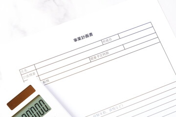 事業計画書 - 新規事業の立ち上げに先立ち、事業計画書を作成する起業家のイメージ
