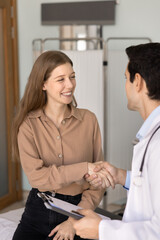 Obraz premium Cheerful young 20s female patient thanking physician for medical consultation, help, advice, shaking hands with practitioner, meeting with doctor after successful effective treatment. Vertical shot