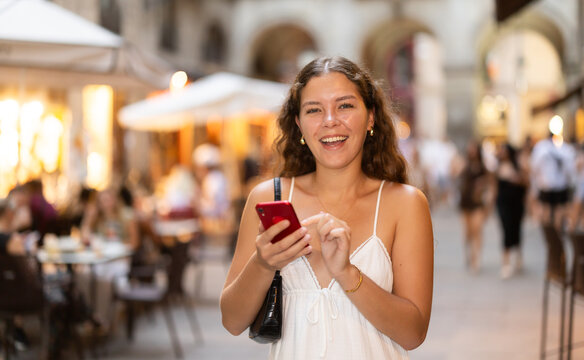Fototapeta Young woman in summer clothes and with a phone in hands walks through the streets of Barcelona, she wants to meet friends and go to a restaurant in the evening