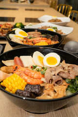 A hearty bowl of seafood noodle soup filled with shrimp, corn, egg, vegetables, rice blood cake, tofu skin, and assorted hotpot ingredients. The colorful ingredients float in a rich broth, making for 