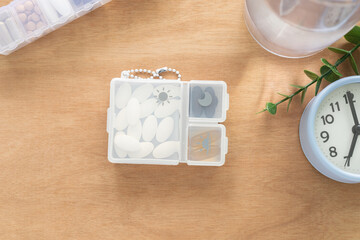 Dietary supplement tablets in plastic box with compartments, water bottle, clock on wooden background, Top view, Health care, pharmacology and minimal medical concept.