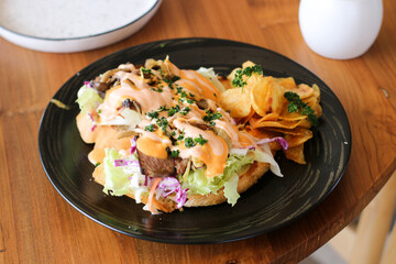 Gourmet Open-Faced Steak Sandwich with Chips on Black Plate, Wooden Table