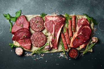 Set of meat and meat products. T-bone steak, ribeye steak, kebab and burger patty. On a black stone background. Top view.