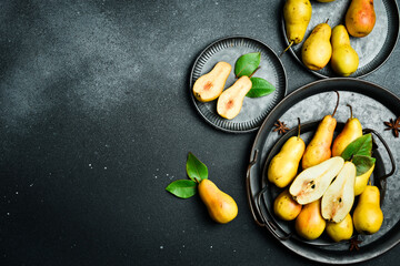 Pears on plates. There are slices of pears and a knife on the cutting board. Top view. On a black stone background.