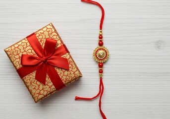 Photo of a golden gift box with a red ribbon and a decorative rakhi bracelet