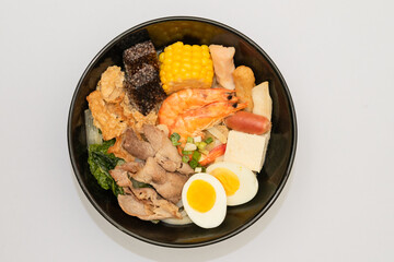 A hearty bowl of seafood noodle soup filled with shrimp, corn, egg, vegetables, rice blood cake, tofu skin, and assorted hotpot ingredients. The colorful ingredients float in a rich broth, making for 