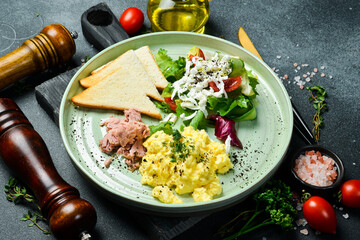 Breakfast. Plate with scrambled eggs, tuna, salad and toast bread. On a black stone background. Free space for text.