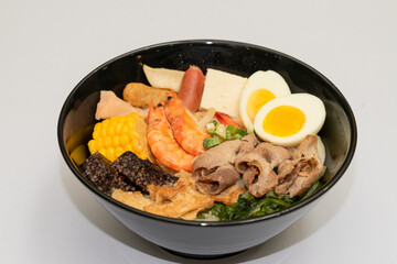 A hearty bowl of seafood noodle soup filled with shrimp, corn, egg, vegetables, rice blood cake, tofu skin, and assorted hotpot ingredients. The colorful ingredients float in a rich broth, making for 