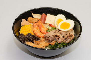 A hearty bowl of seafood noodle soup filled with shrimp, corn, egg, vegetables, rice blood cake, tofu skin, and assorted hotpot ingredients. The colorful ingredients float in a rich broth, making for 