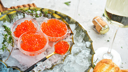 Red salmon caviar in small bowls on ice. Gourmet food in a restaurant. On concrete texture background.