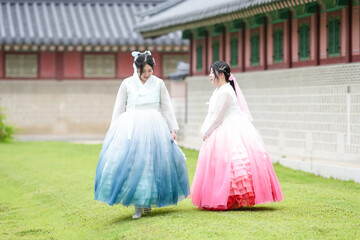 Two Korean women in their twenties walk across a grassy lawn before a historic hall at...