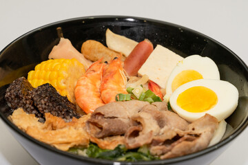 A hearty bowl of seafood noodle soup filled with shrimp, corn, egg, vegetables, rice blood cake, tofu skin, and assorted hotpot ingredients. The colorful ingredients float in a rich broth, making for 
