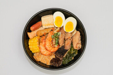 A hearty bowl of seafood noodle soup filled with shrimp, corn, egg, vegetables, rice blood cake, tofu skin, and assorted hotpot ingredients. The colorful ingredients float in a rich broth, making for 