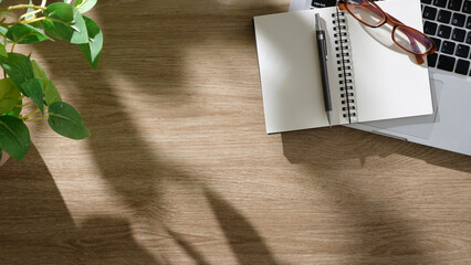 Minimalist desk with an open notebook, pen, and laptop under soft natural light.