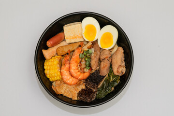 A hearty bowl of seafood noodle soup filled with shrimp, corn, egg, vegetables, rice blood cake, tofu skin, and assorted hotpot ingredients. The colorful ingredients float in a rich broth, making for 