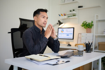 Pensive businessman thinking deeply while sitting at a modern office desk with a laptop and documents.