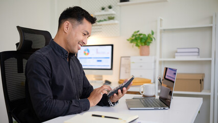 Smiling businessman calculating data with a calculator at a clean, modern office desk.