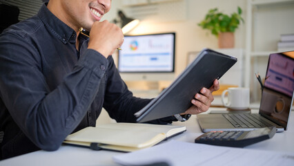 Close-up of a cheerful businessman analyzing documents with a pen in hand, working in a modern...