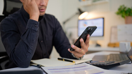 Close-up of a concerned businessman looking at his smartphone in the office, possibly reading bad news or an urgent message.