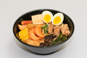 A hearty bowl of seafood noodle soup filled with shrimp, corn, egg, vegetables, rice blood cake, tofu skin, and assorted hotpot ingredients. The colorful ingredients float in a rich broth, making for 