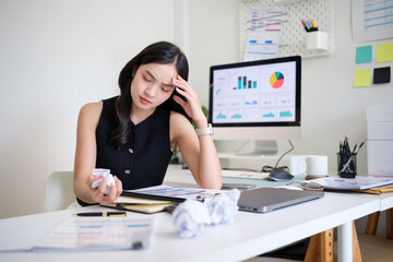 Frustrated businesswoman holding her head and crumpled paper, struggling with work pressure.