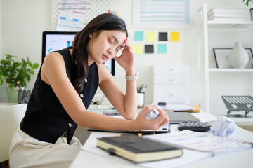 Frustrated businesswoman holding crumpled paper while feeling stressed at desk.
