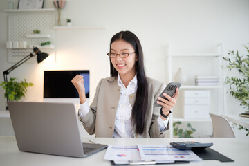 Happy accountant holding a smartphone and raising a fist after completing financial tasks.