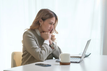 Thoughtful businesswoman staring at laptop screen, focusing on important tasks in a quiet office.