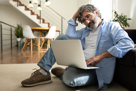 Mature man relaxing at home, sitting on the floor using laptop.