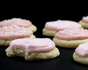 Colorful heart-shaped cookies with pink frosting and sprinkles are displayed on a dark background, inviting sweet cravings for treats
