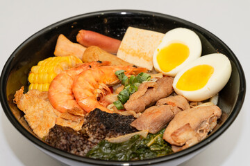 A hearty bowl of seafood noodle soup filled with shrimp, corn, egg, vegetables, rice blood cake, tofu skin, and assorted hotpot ingredients. The colorful ingredients float in a rich broth, making for 