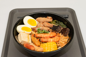 A hearty bowl of seafood noodle soup filled with shrimp, corn, egg, vegetables, rice blood cake, tofu skin, and assorted hotpot ingredients. The colorful ingredients float in a rich broth, making for 