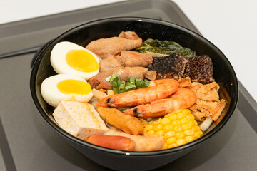 A hearty bowl of seafood noodle soup filled with shrimp, corn, egg, vegetables, rice blood cake, tofu skin, and assorted hotpot ingredients. The colorful ingredients float in a rich broth, making for 