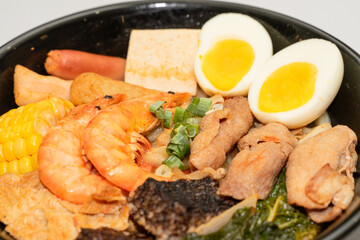 A hearty bowl of seafood noodle soup filled with shrimp, corn, egg, vegetables, rice blood cake, tofu skin, and assorted hotpot ingredients. The colorful ingredients float in a rich broth, making for 