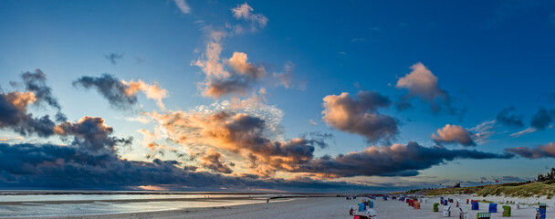 Durch die untergehende Sonne angestrahlte Wolkenfetzen über der Nordsee am Strand von Utersum auf...