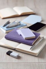 Assorted stationery and tech items on a light wood surface.  Open notebooks, pens, a tablet, and a USB drive are visible