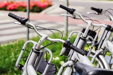 Urban rental bicycles parked. Public city bike station on sidewalk. Closeup of handlebars and...