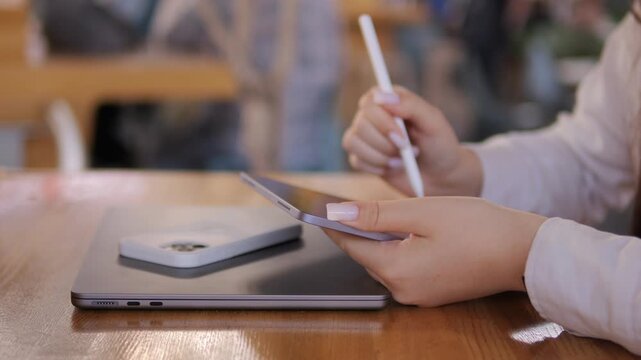 Woman is sitting at a table with a laptop and a cell phone. She is holding a pen and writing on a piece of paper