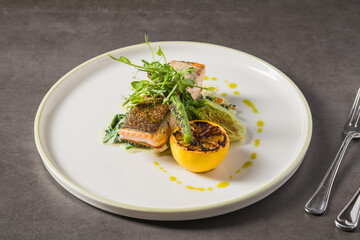 Grilled salmon fillet with charred lemon and greens on plate