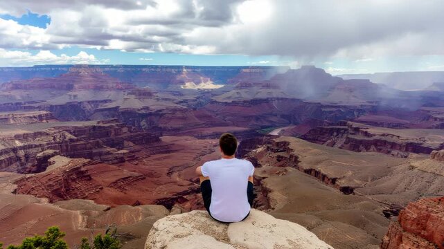 Majestic Grand Canyon Vista: Man Contemplates Epic Landscape Under Dynamic Skies with Distant Rain