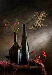 Still life with hot pepper, glass bottles and a dry branch on a dark background