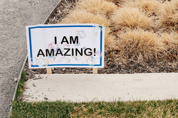 Sign expressing positivity and encouragement in a landscaped area during daylight, featuring...