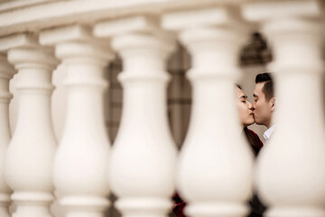 A romantic moment captured through classic white balusters, showing an Asian couple sharing a tender kiss, symbolizing love, intimacy, and connection.