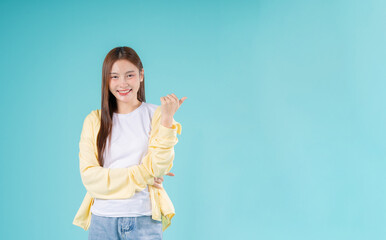 Cheerful young Asian woman pointing to the side while smiling against a turquoise background,...