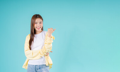 Cheerful young Asian woman pointing to the side while smiling against a turquoise background,...