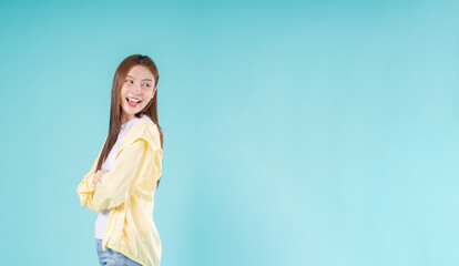 Smiling young Asian woman looking to the side with crossed arms against a blue background, perfect...