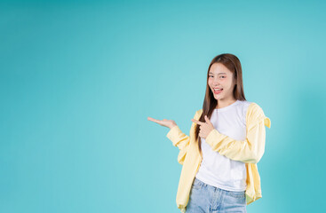 Happy young Asian woman pointing at open hand with a smile against a blue background, perfect for...